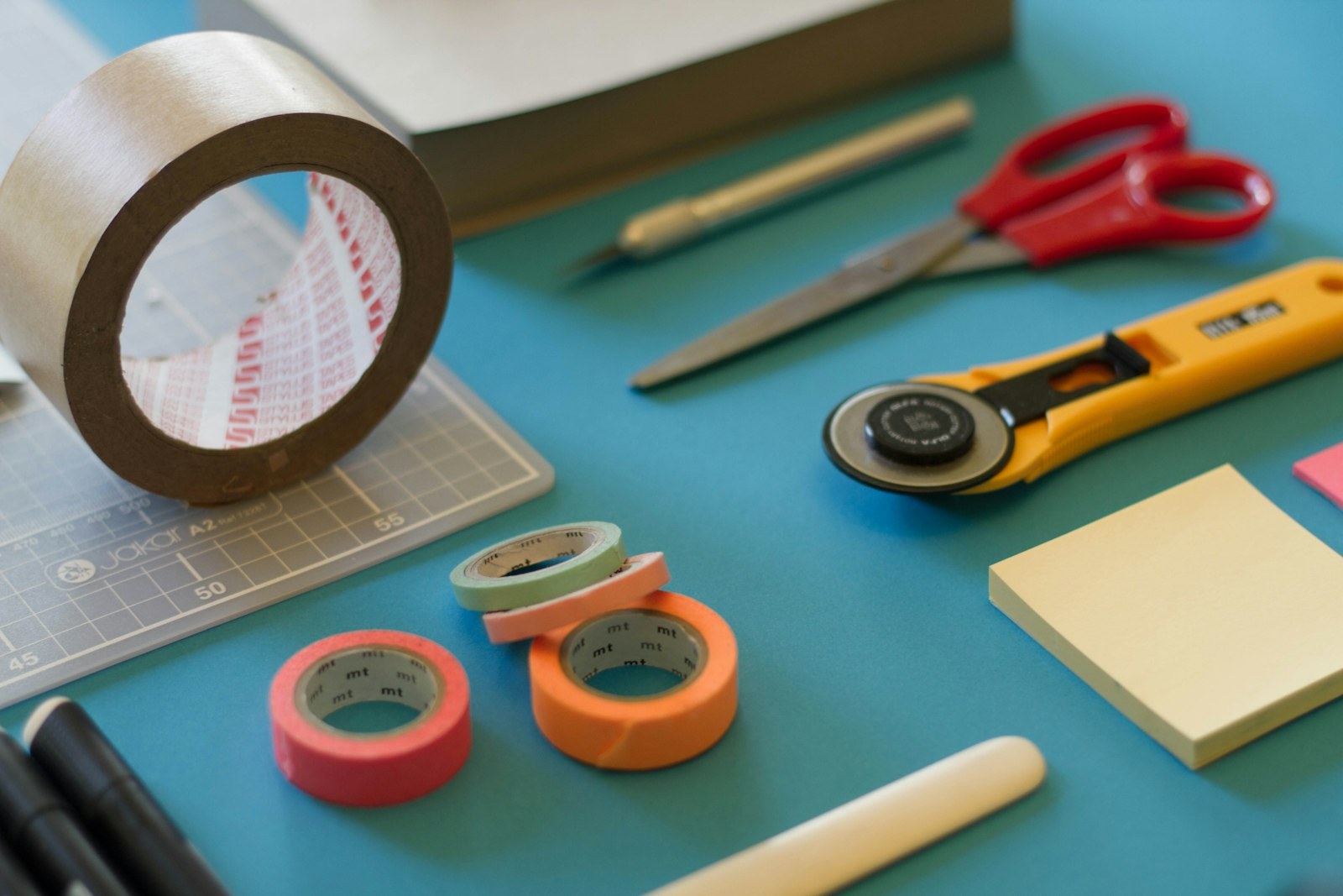 Craft tools including a rotary cutter, scissors, and tape on a teal surface