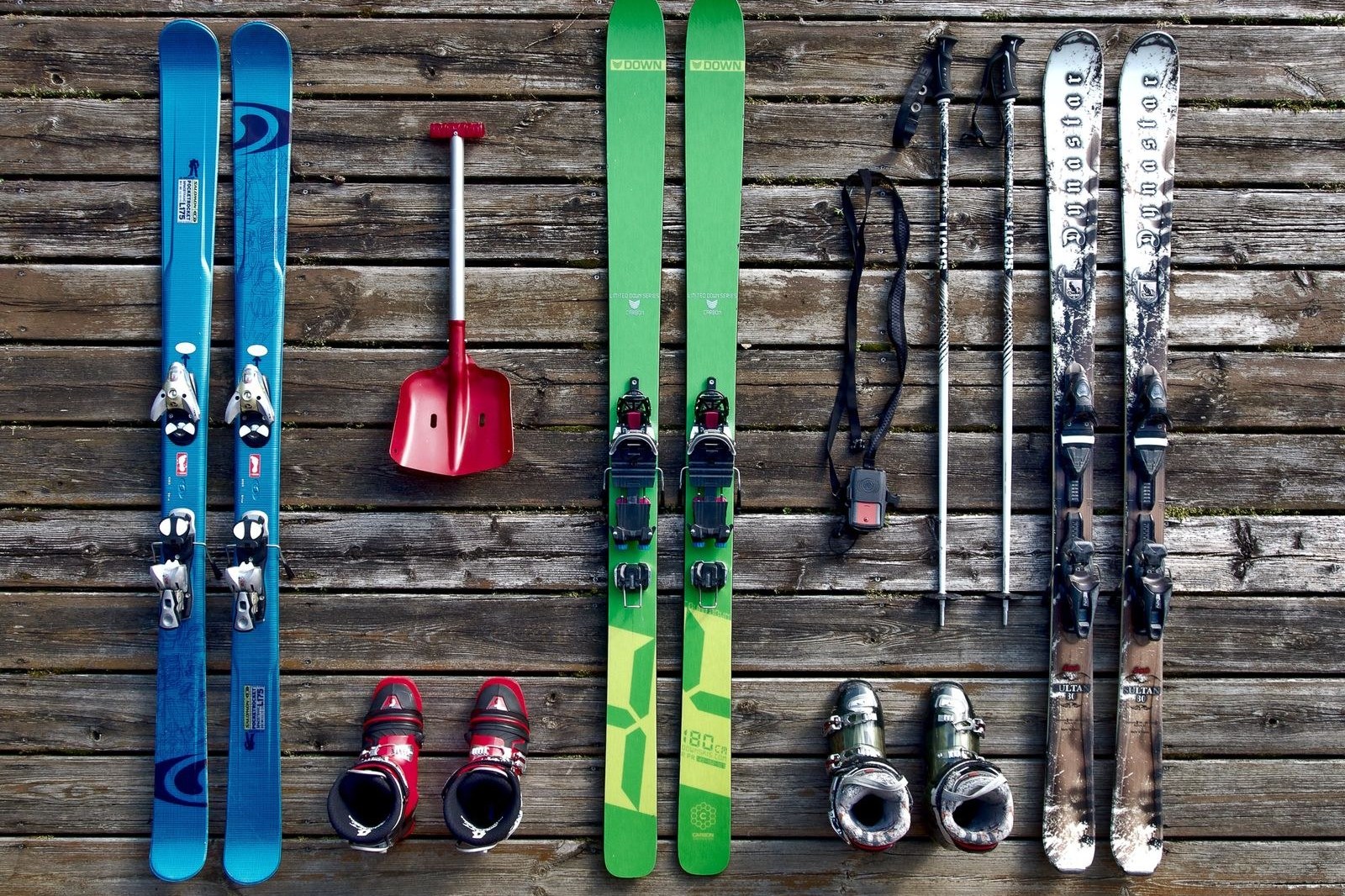 Ski pairs, boots, poles, and avalanche gear laid out on a wooden deck