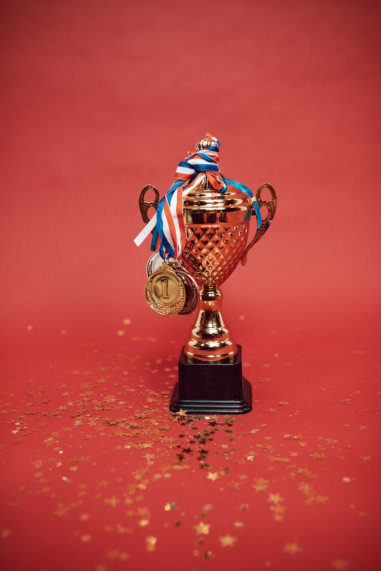 A gold trophy cup with medals on red, white and blue ribbons against a red background