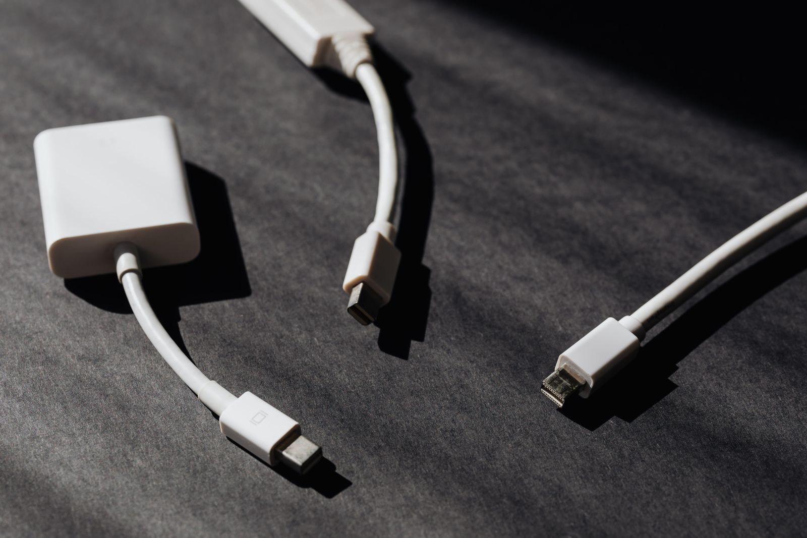 White adapters and short cables on a dark textured surface with sharp shadows