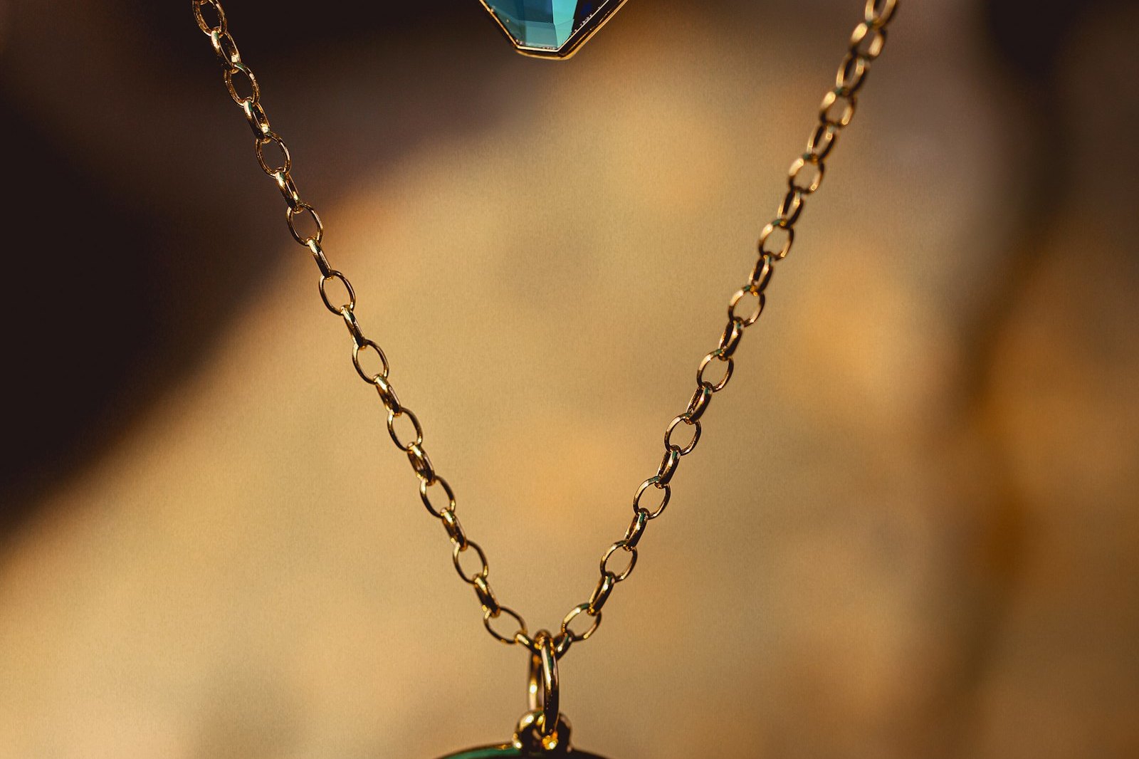 Two gold necklaces hanging in front of a warm background, one with a blue stone and one with a crescent pendant