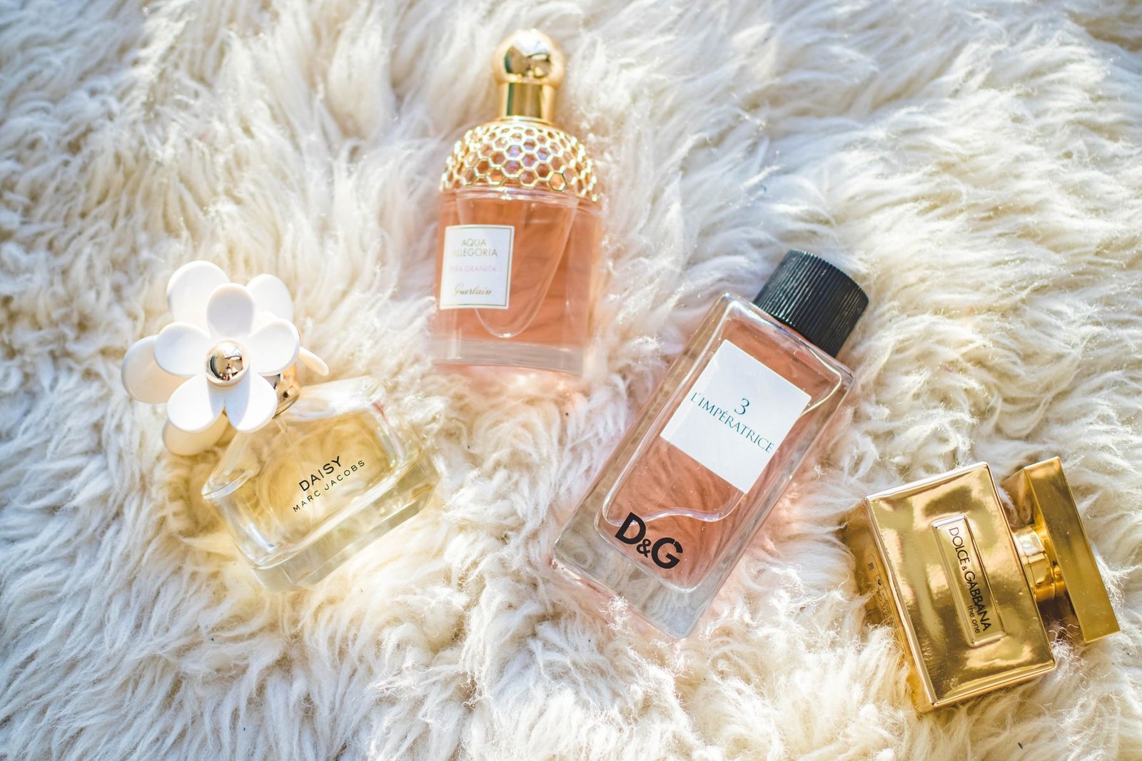 Flere parfumeflasker arrangeret på en blød cremefarvet overflade