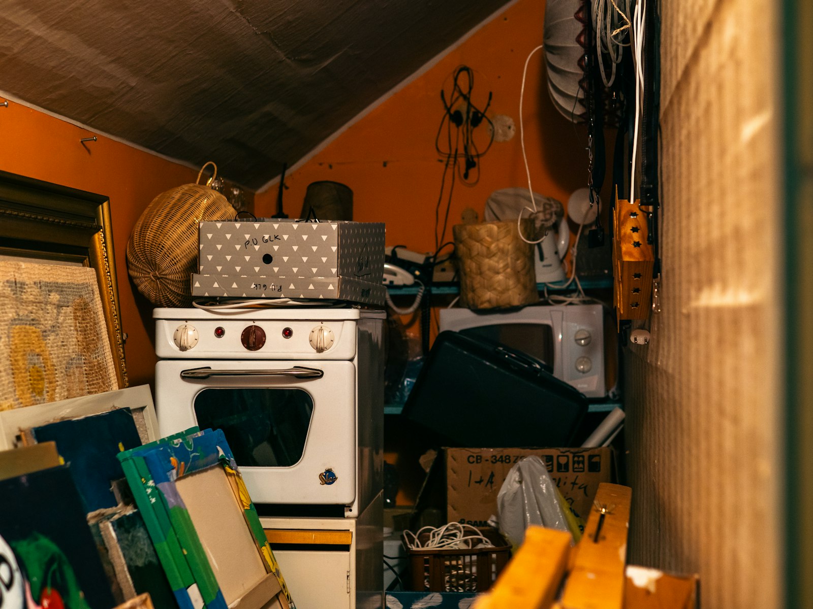 An attic storage room crowded with an old stove, framed paintings and boxes of belongings