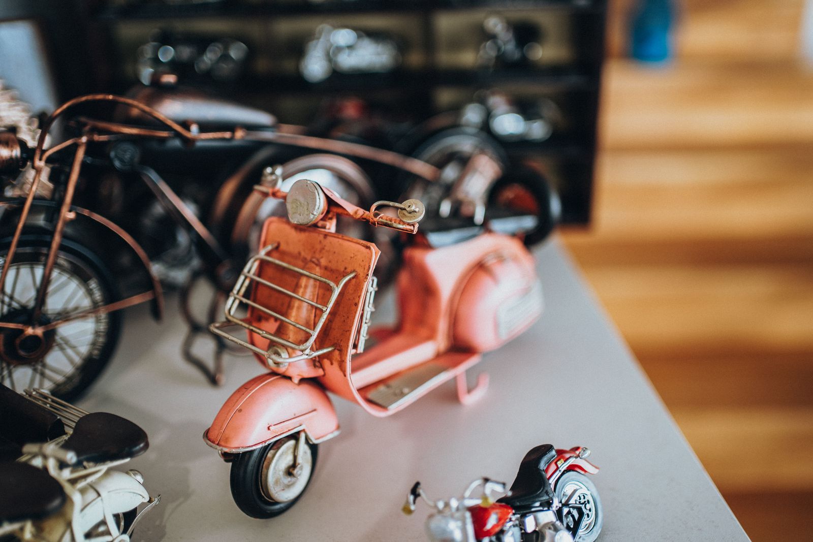 A vintage pink tin toy scooter and old toy motorcycles on a shelf