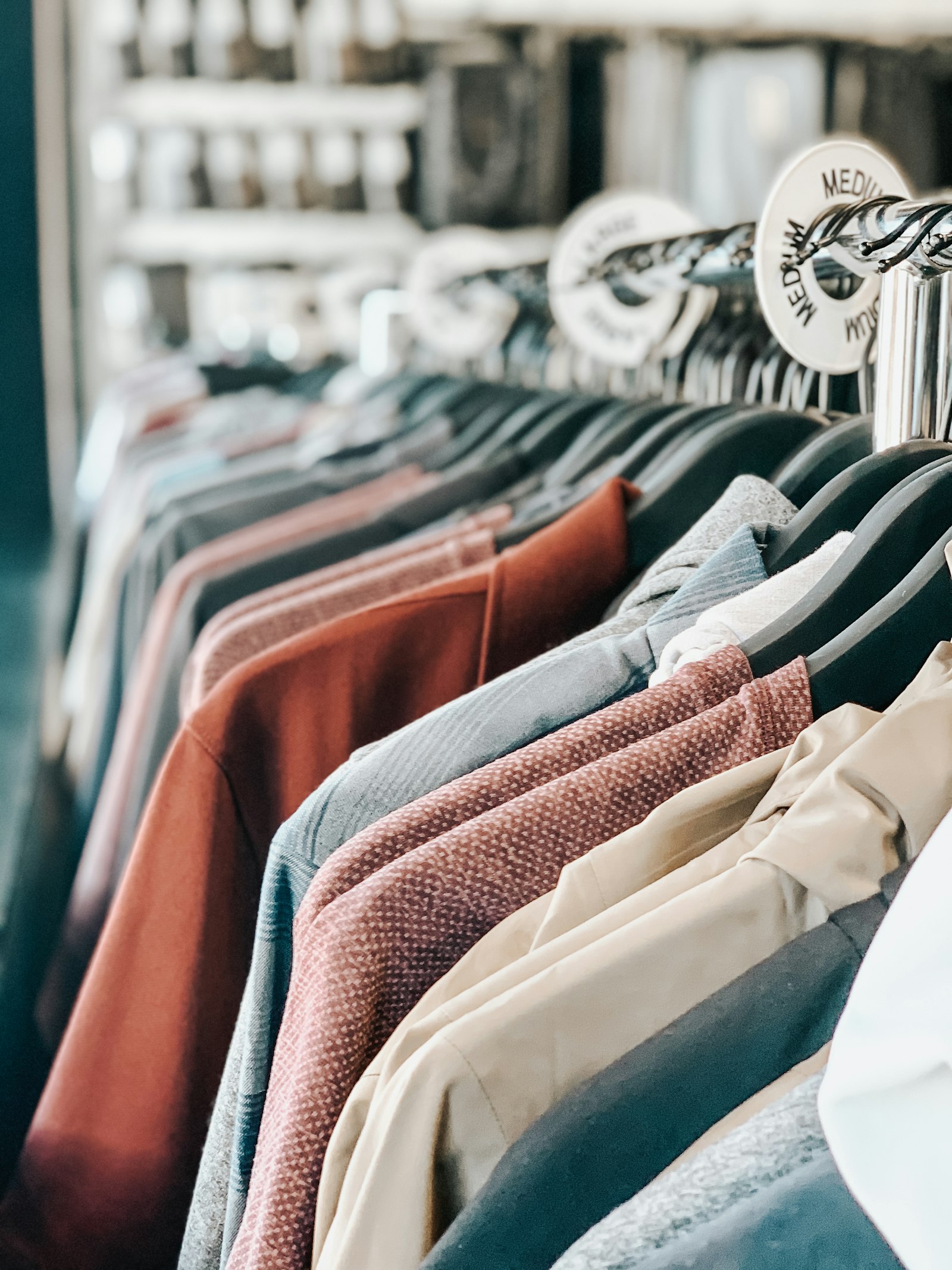 A clothing rack of jackets and sweaters on black hangers with a MEDIUM size divider