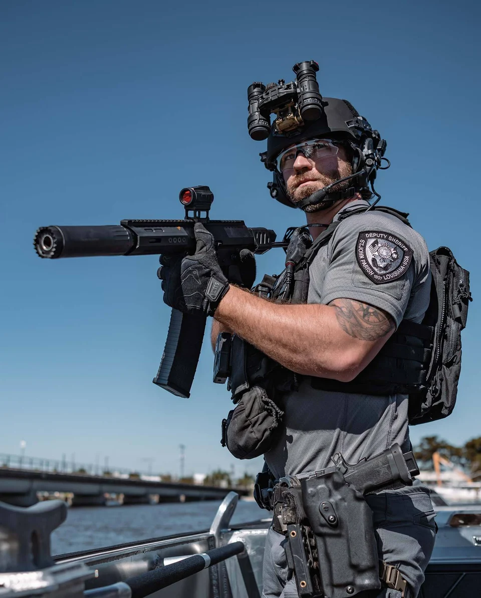 Person wearing a helmet and tactical equipment holding a firearm in an official Genesis Arms photograph