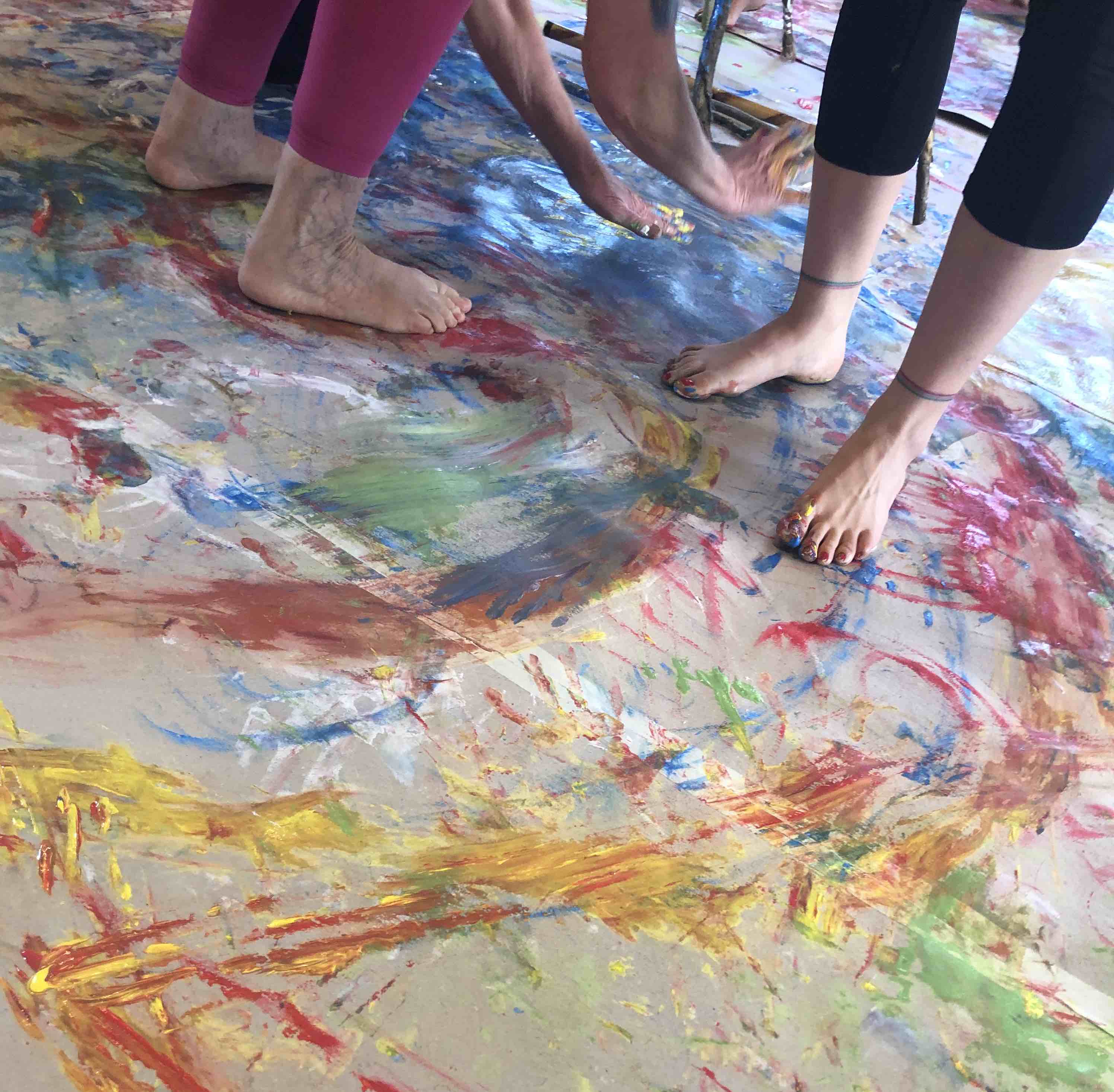 Bunt bemalte nackte Füße auf einer mit Farbe bespritzten Malunterlage bei einer kreativen Biodanza-Vivencia
