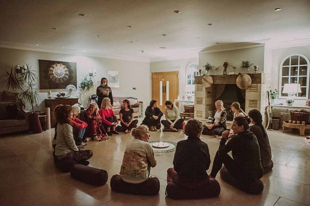 A group of people sitting in a circle on the floor in a well-lit room, engaged in a discussion or activity.