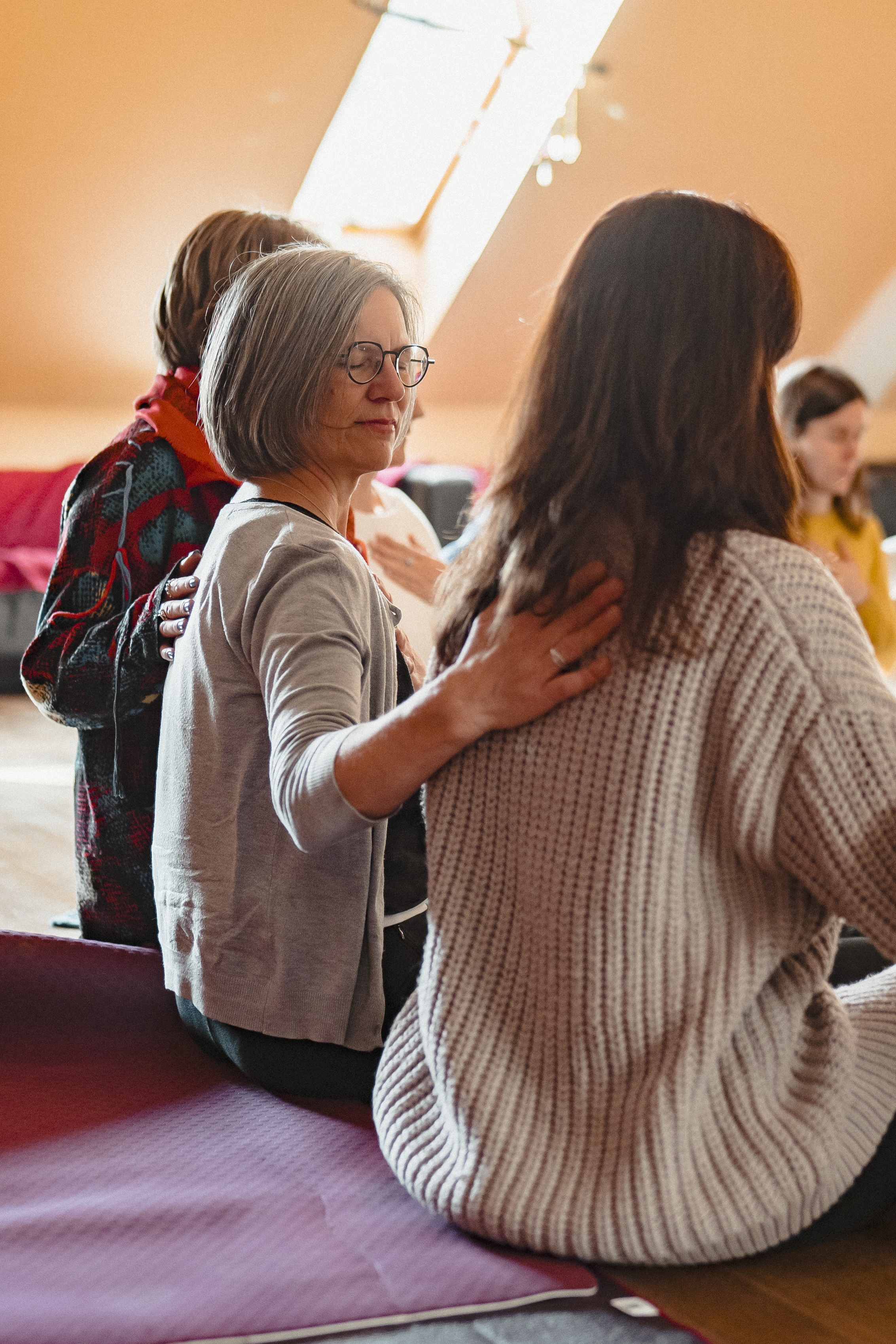 Ein Frau legt im Closing Circle einer anderen Frau die Hand auf den Rücken. Sie hat die Augen sanft geschlossen. Es ist ein Moment der Verbindung.