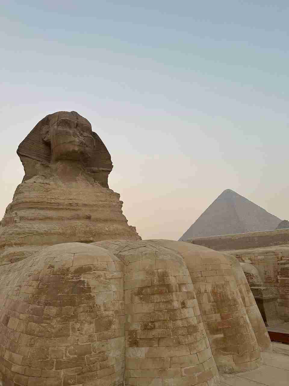 Die Sphinx steht vor einer Pyramide und der Himmel ist in sanften Farbtönen.
