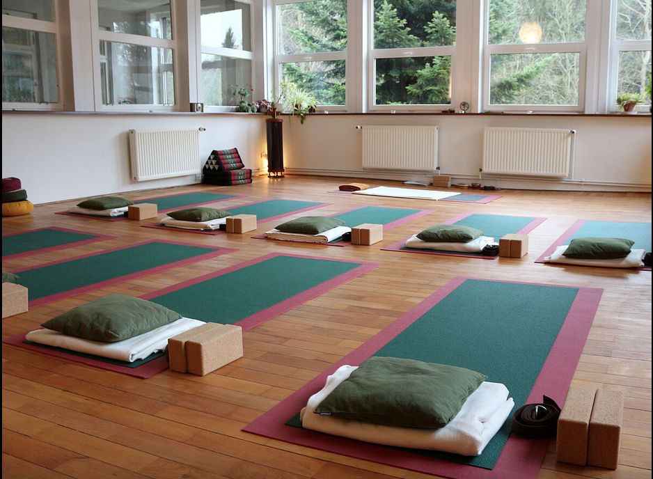 Ein großer, heller Raum mit Yoga-Matten und Kissen auf dem Fußboden.