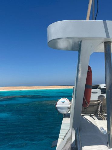 Ein Blick von einem Boot auf das blaue Wasser und einen Strand im Hintergrund.