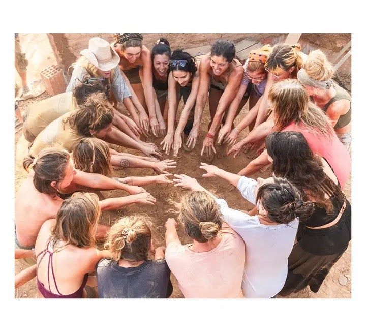 A group of women with hands in a circle, engaged in a collaborative activity with dirt.