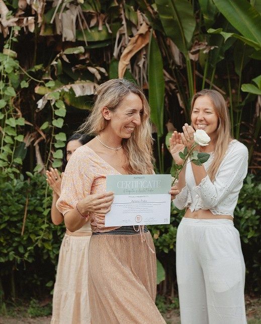 A woman happily receiving a certificate with others applauding her in a garden.