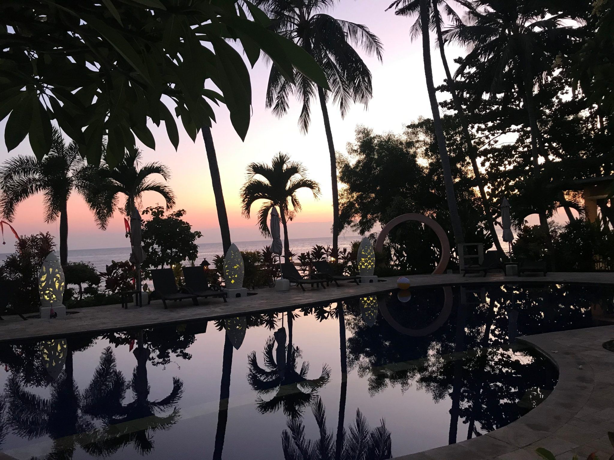 Ein Pool umgeben von Palmen bei Sonnenuntergang.