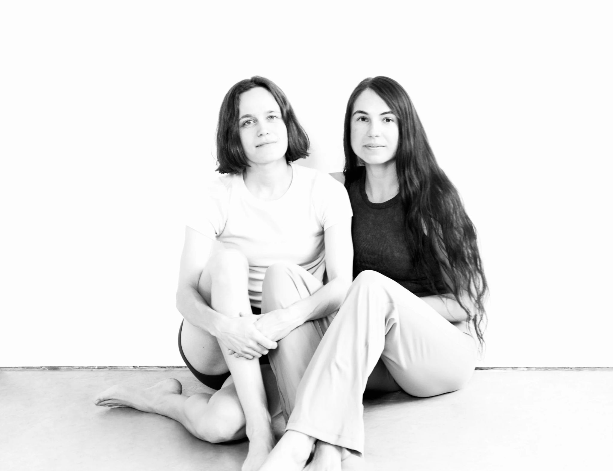 Das Bild zeigt zwei Frauen, die auf dem Boden sitzen und in die Kamera blicken.