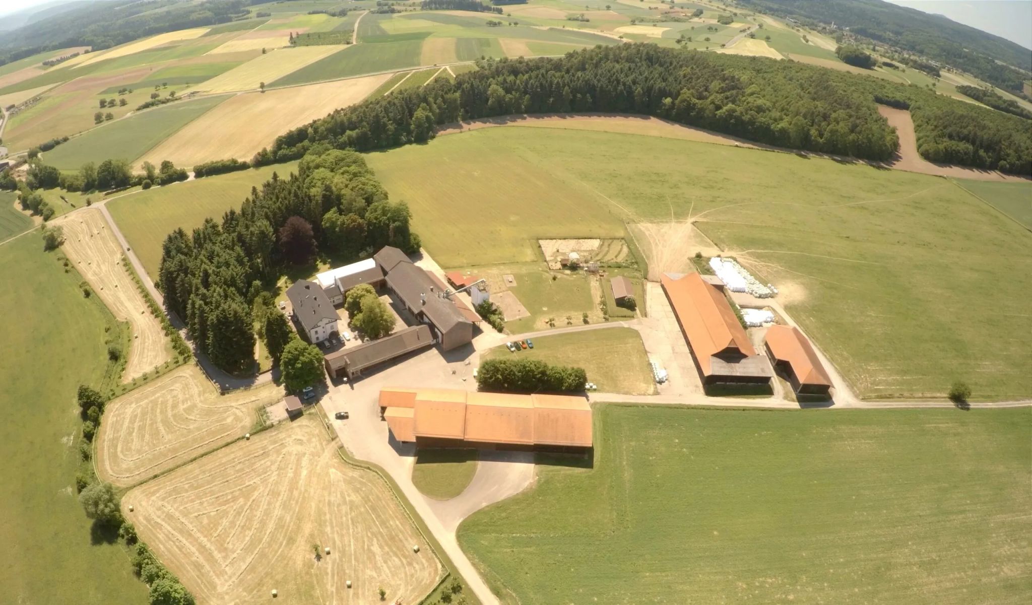 Eine Luftaufnahme eines großen Geländes mit Feldern und Wäldern ist sichtbar.