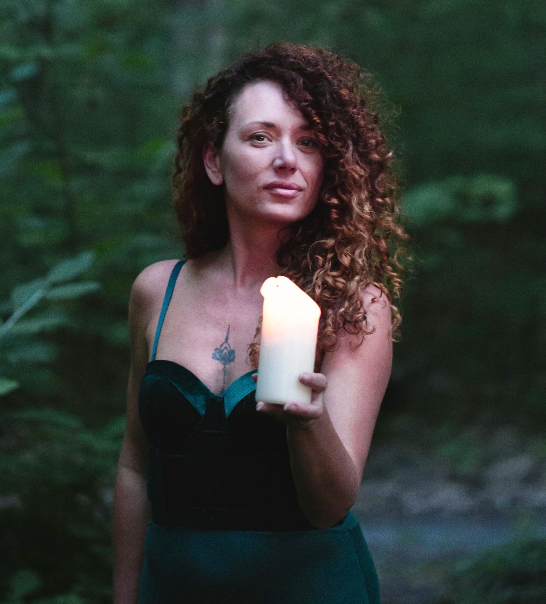 A woman standing in a forest holding a lit candle.