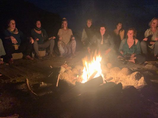 Eine Gruppe von Personen sitzt um ein Lagerfeuer.