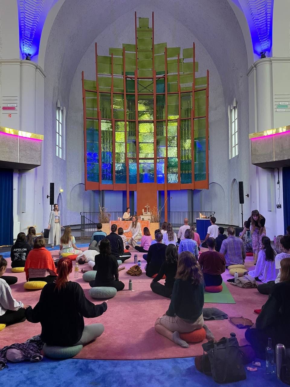 Gruppe sitzt in einer Kirche, im Hintergrund die Orgel, beleuchtet in warmen und blauen Farbtönen.