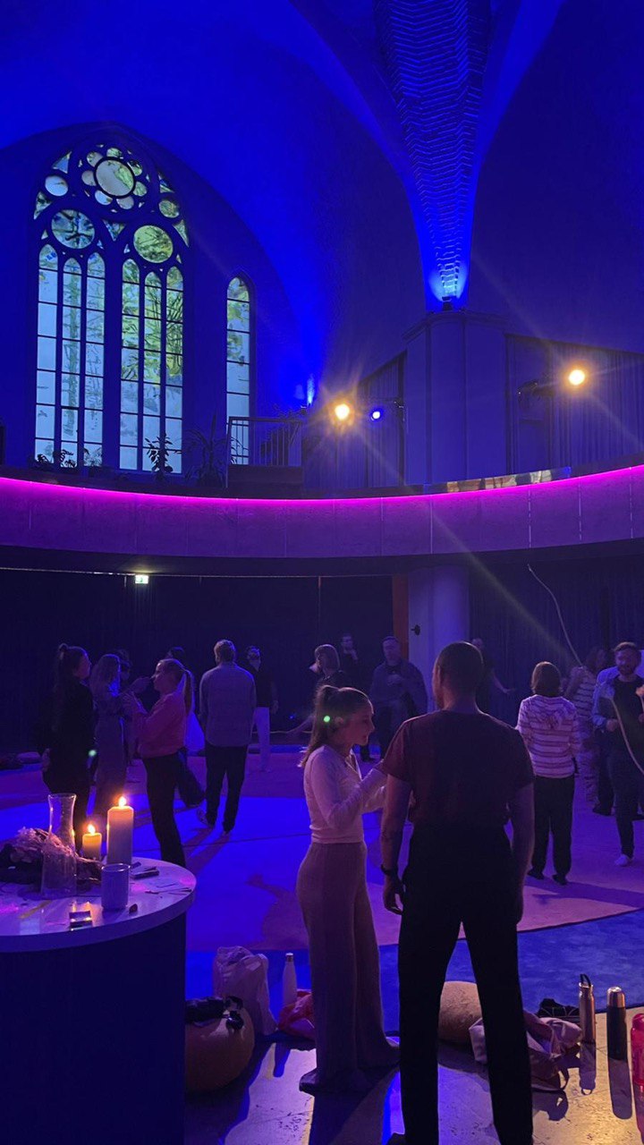 Menschen stehen im Kirchenraum, Silhouetten vor pinkem und violettem Licht.