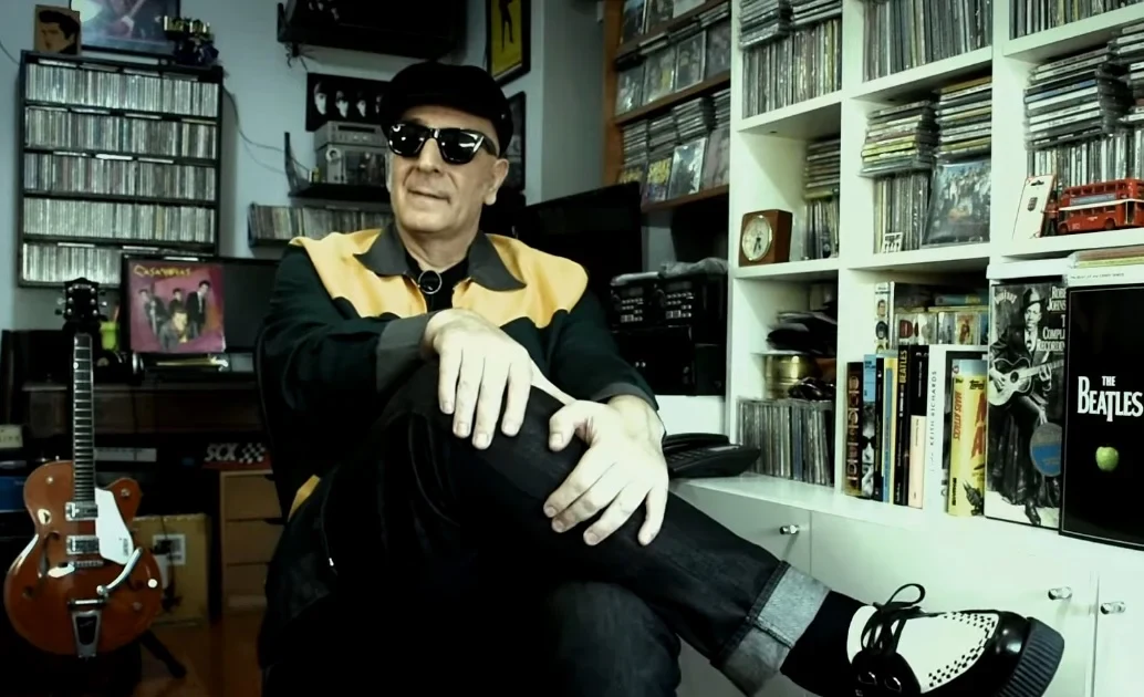 Flavio Casanova con anteojos oscuros y guantes blancos, sentado frente a una biblioteca de discos, en Casanovas, un disco de culto