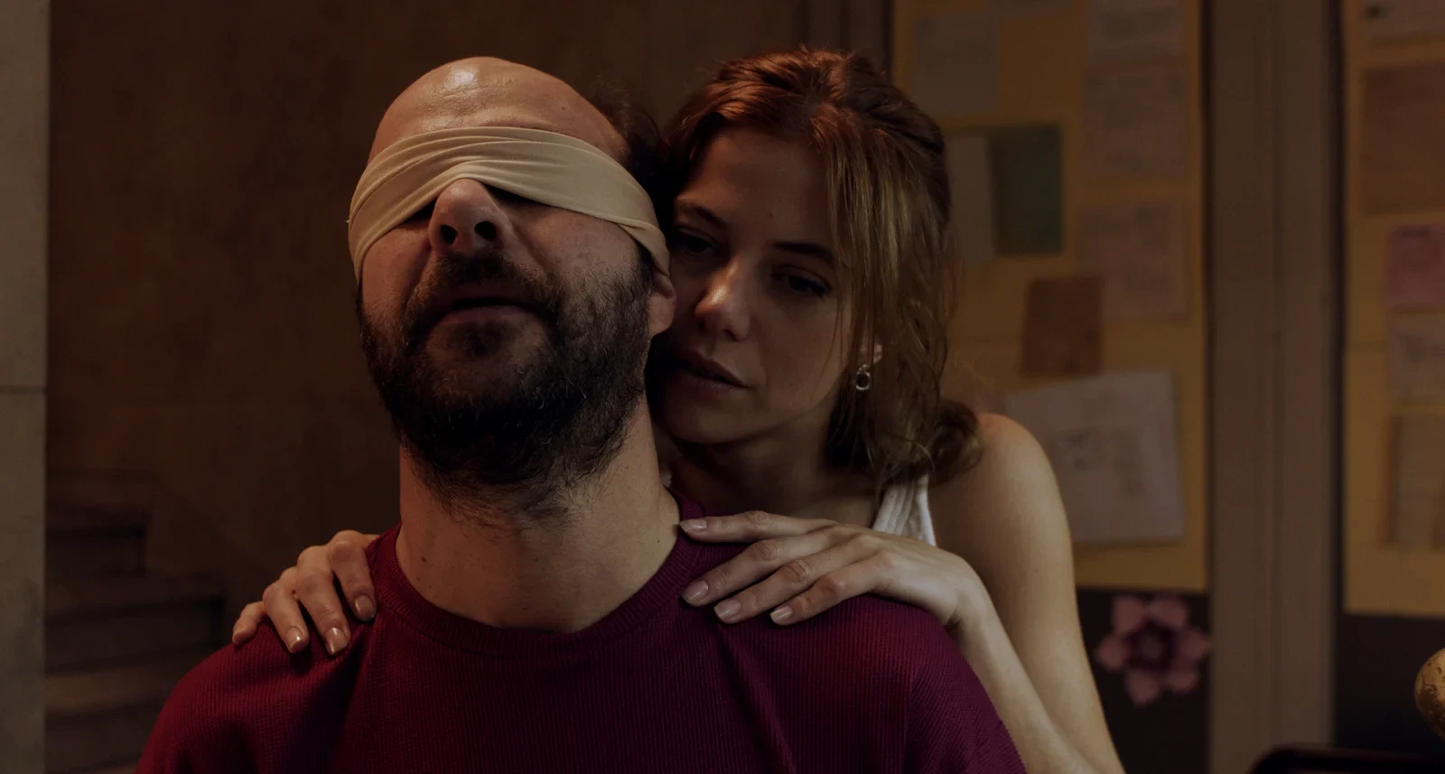 Una mujer abraza por detrás a un hombre con los ojos vendados