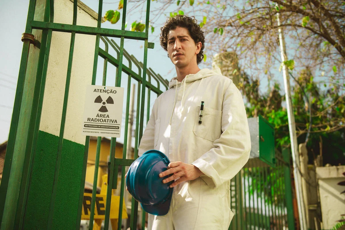 Un hombre joven con ropa blanca de protección junto a un portón con señal de radiación