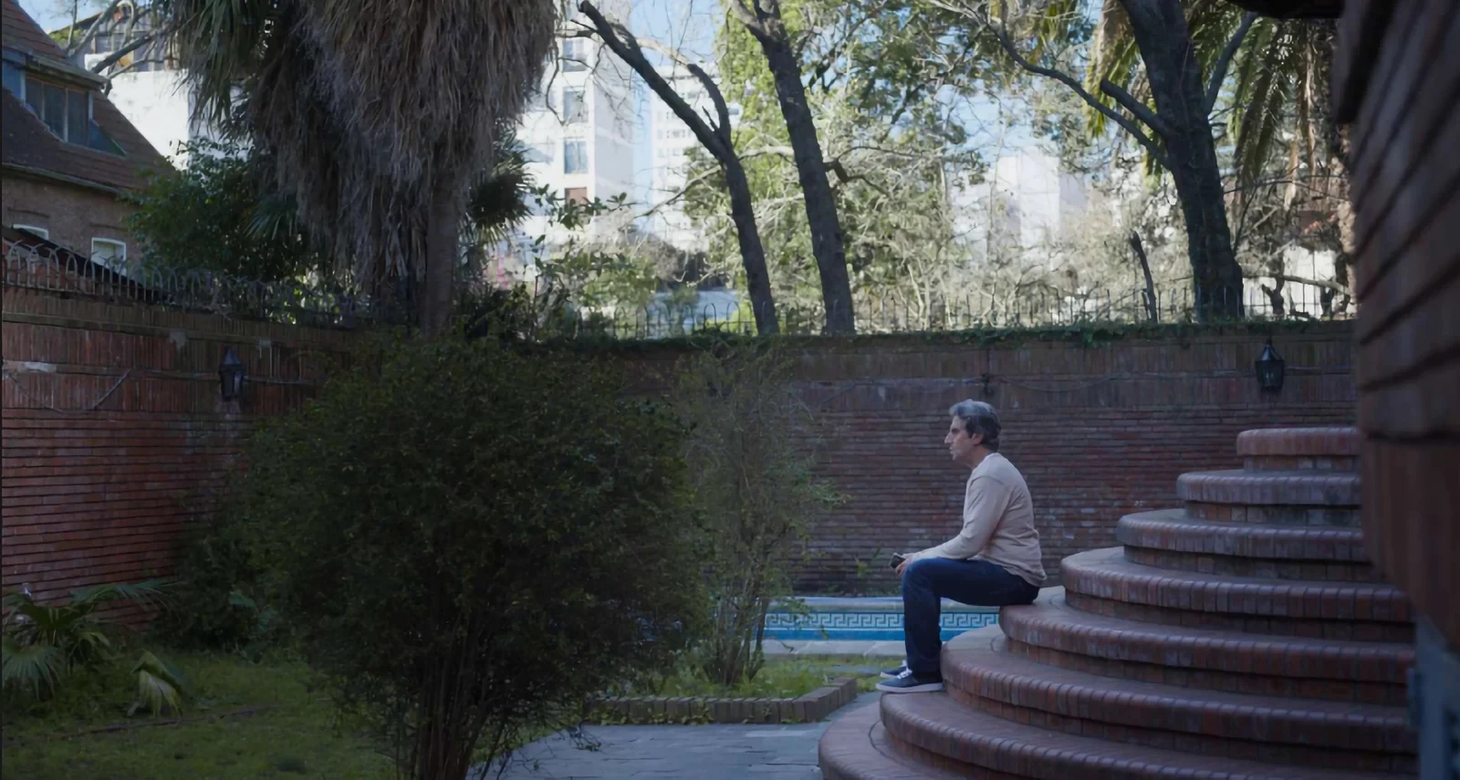 Diego Peretti sentado en la escalera del jardín de una casa grande, en La casa