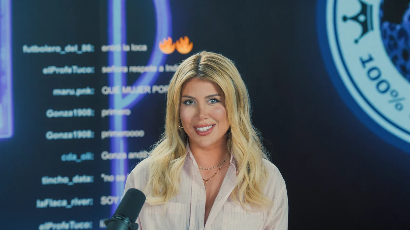 Wanda Nara sonriente en un set con pantallas de redes sociales