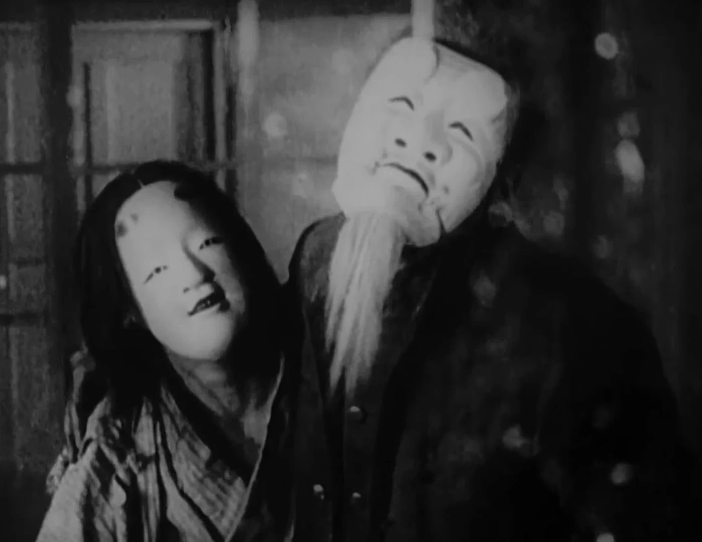 Un hombre con una máscara noh de anciano junto a una interna que también lleva máscara, en A Page of Madness
