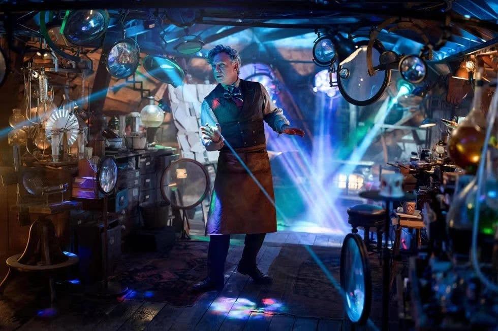 Daniel Craig con delantal de trabajo en un taller lleno de aparatos y luces, en Narnia: El sobrino del mago