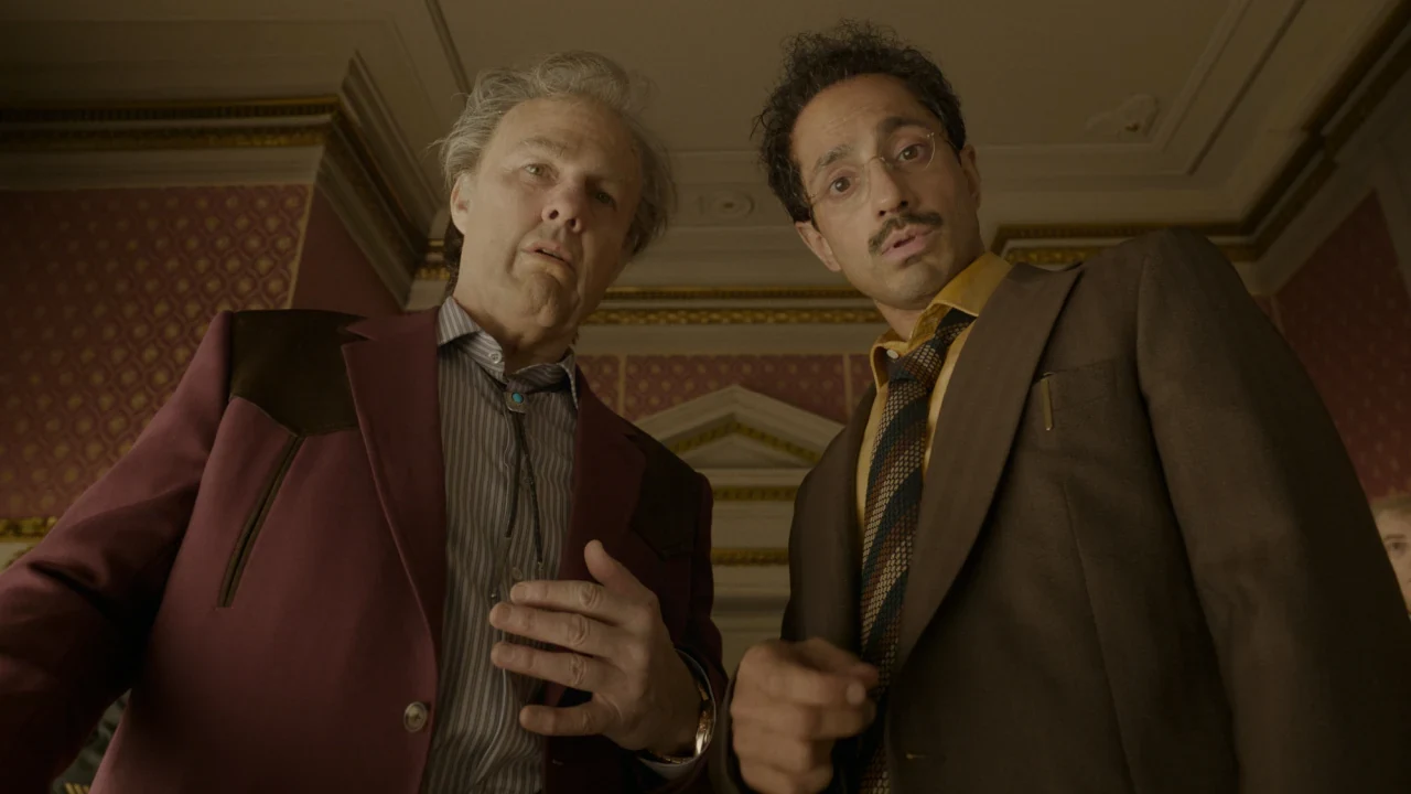 Tom Cruise como Rockwell, de traje bordó, junto a Riz Ahmed en un salón de Digger
