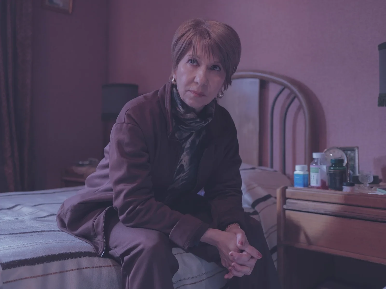Alejandra Flechner sentada en el borde de una cama, en un cuarto de paredes rosadas
