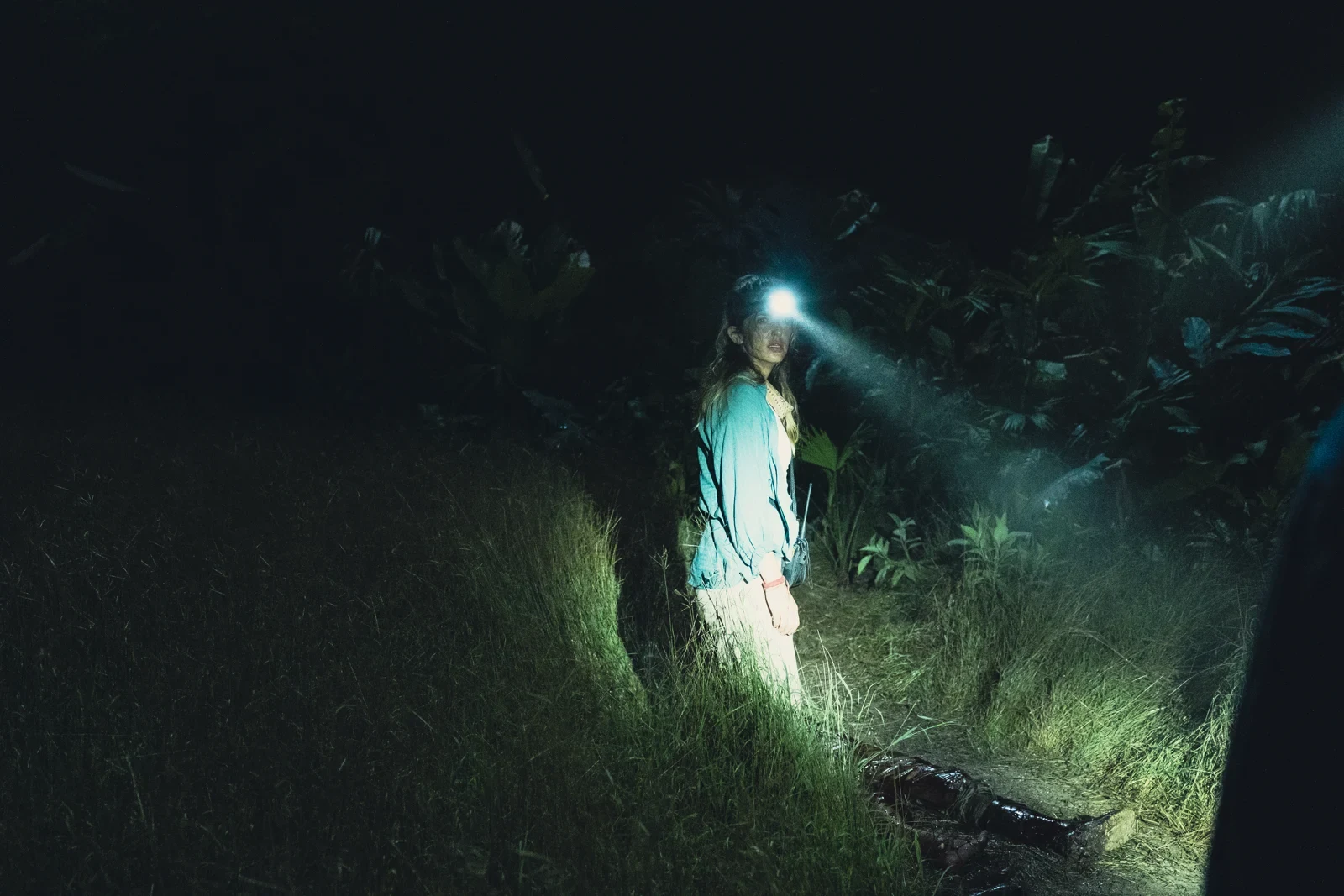 Una figura con linterna en la selva nocturna