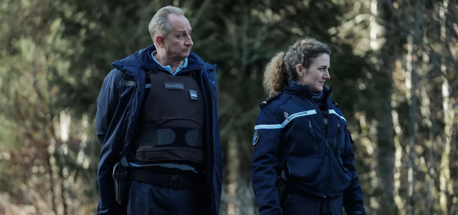 Benoît Poelvoorde con uniforme de gendarme junto a Joséphine de Meaux en un bosque, en Misterioso asesinato en la montaña