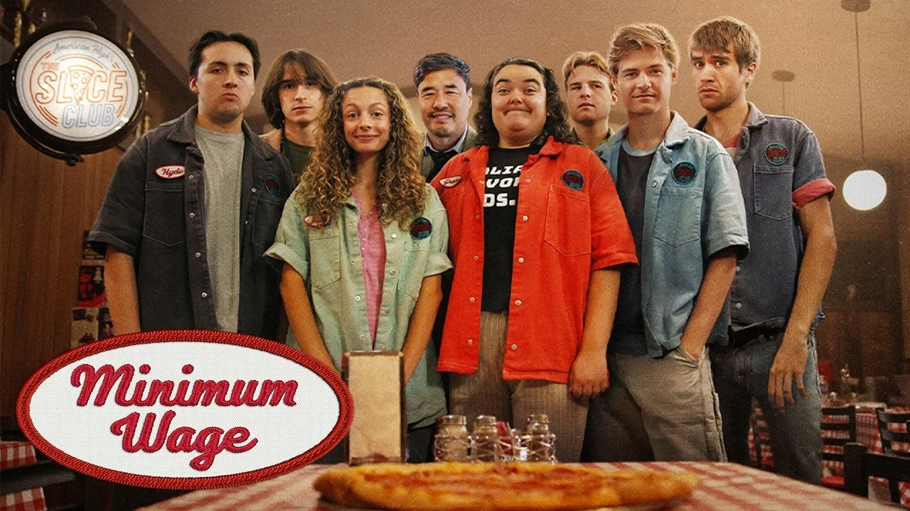 Elenco de Salario mínimo detrás del mostrador con una pizza en primer plano