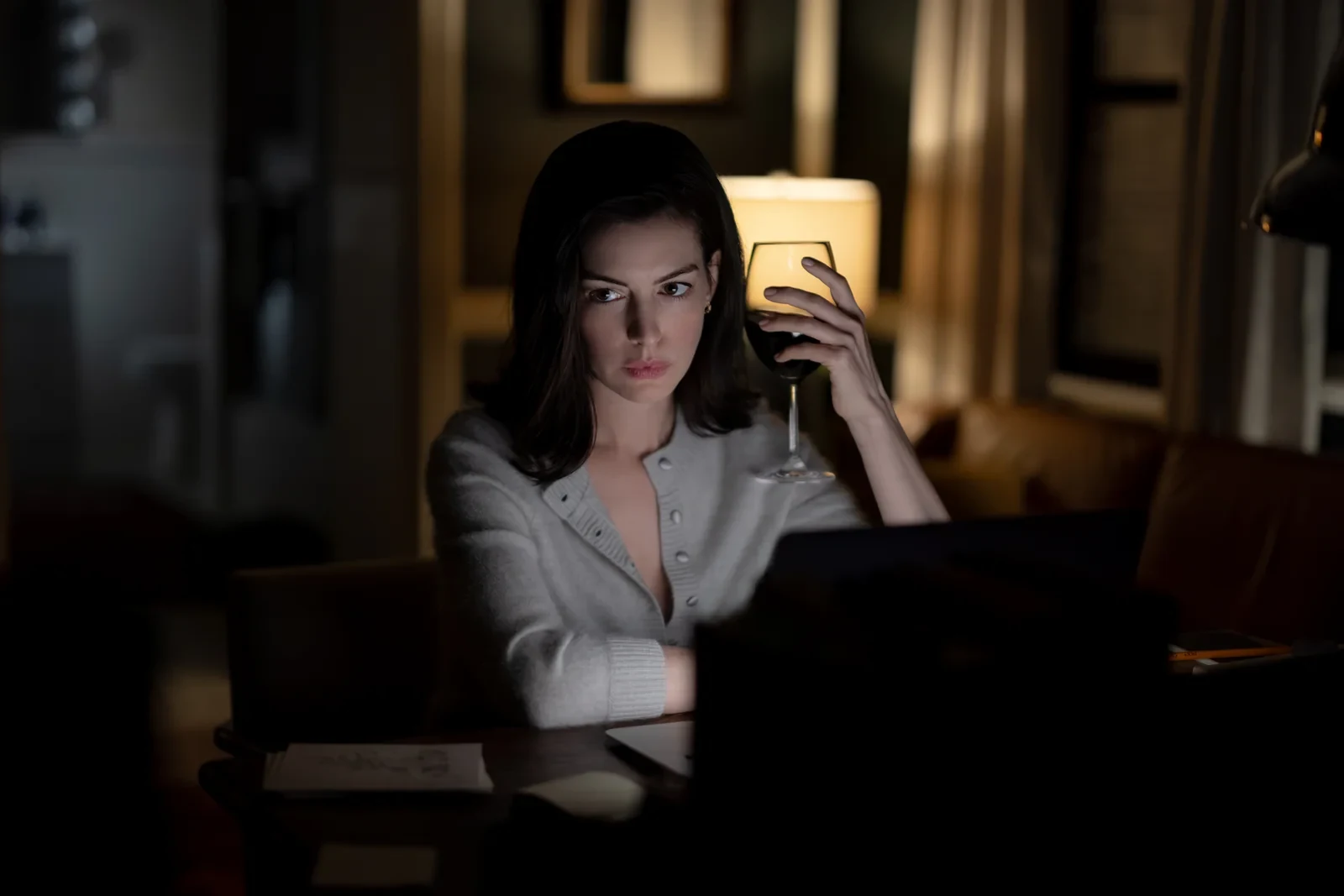 Anne Hathaway con una copa de vino frente a una computadora en Verity: La sombra del engaño