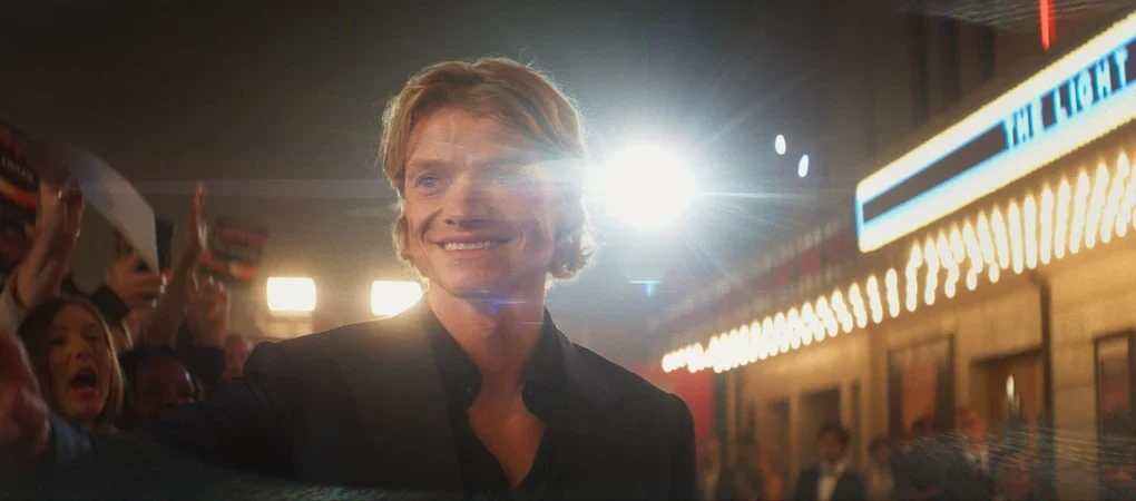 Un hombre sonriente frente a la marquesina iluminada de un cine