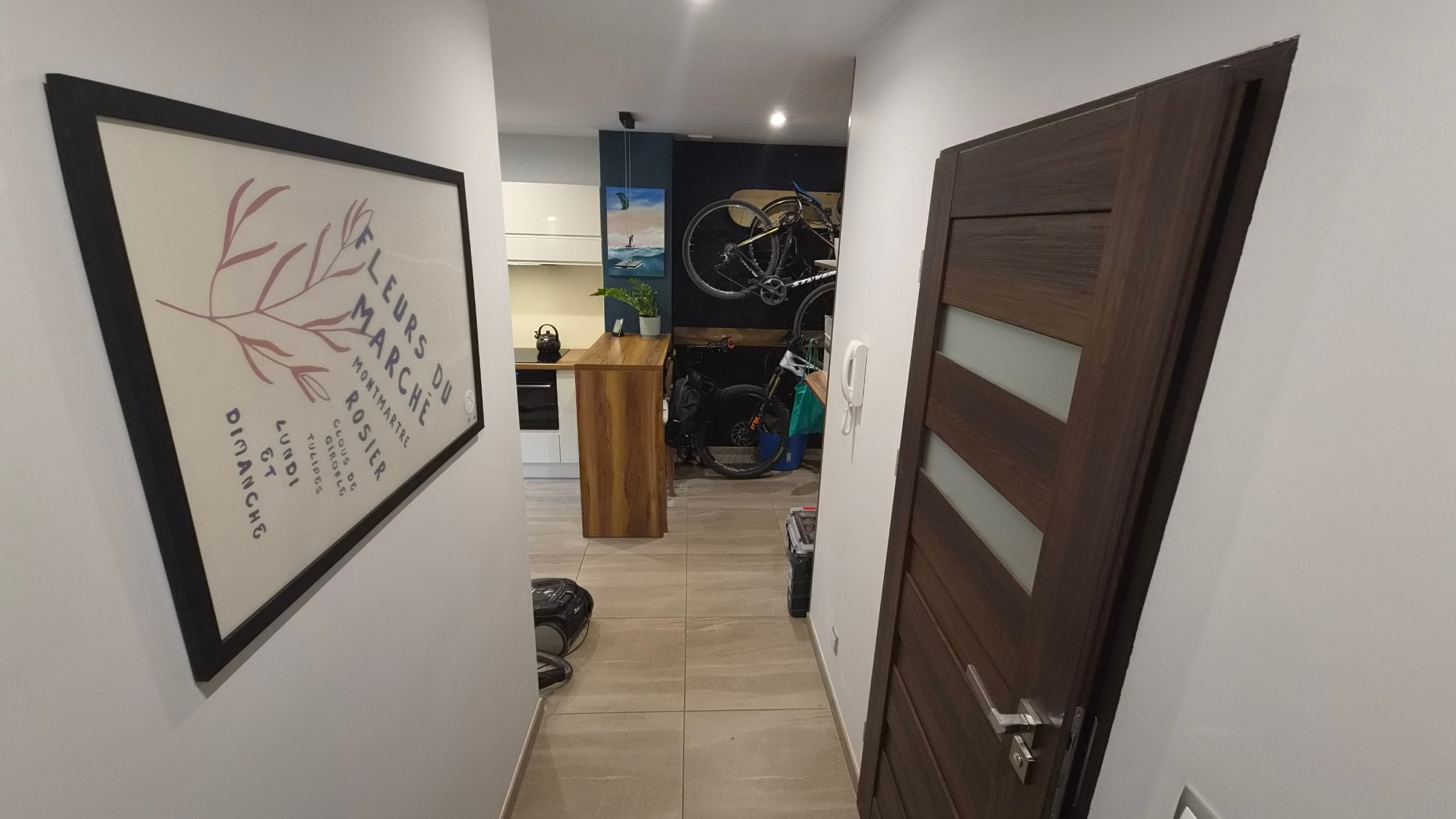 Przedpokój z plakatem w ramie; w głębi aneks kuchenny i ściana z rowerami