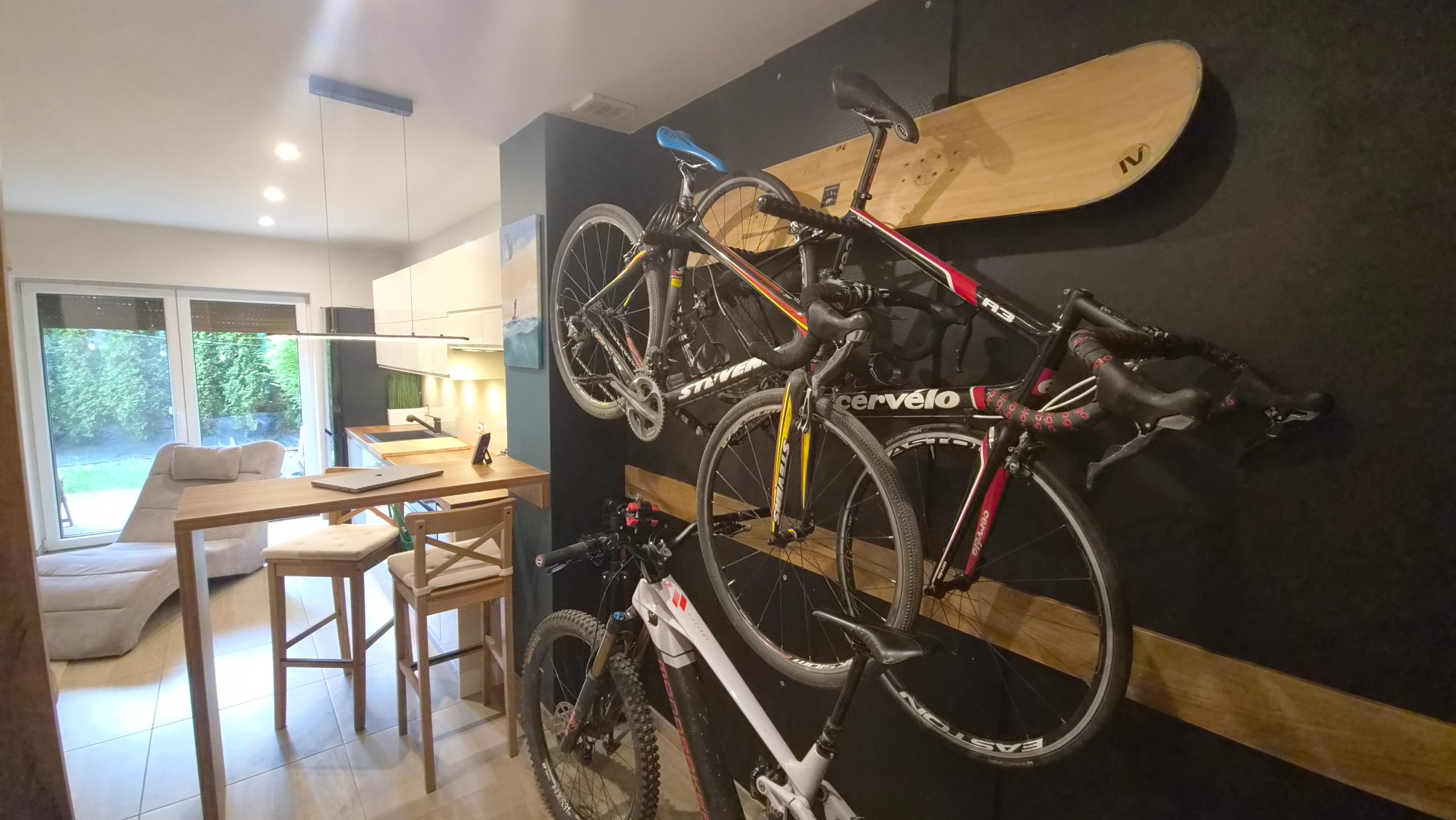 Ściana z rowerami i deską snowboardową; w tle salon z wyjściem do ogrodu