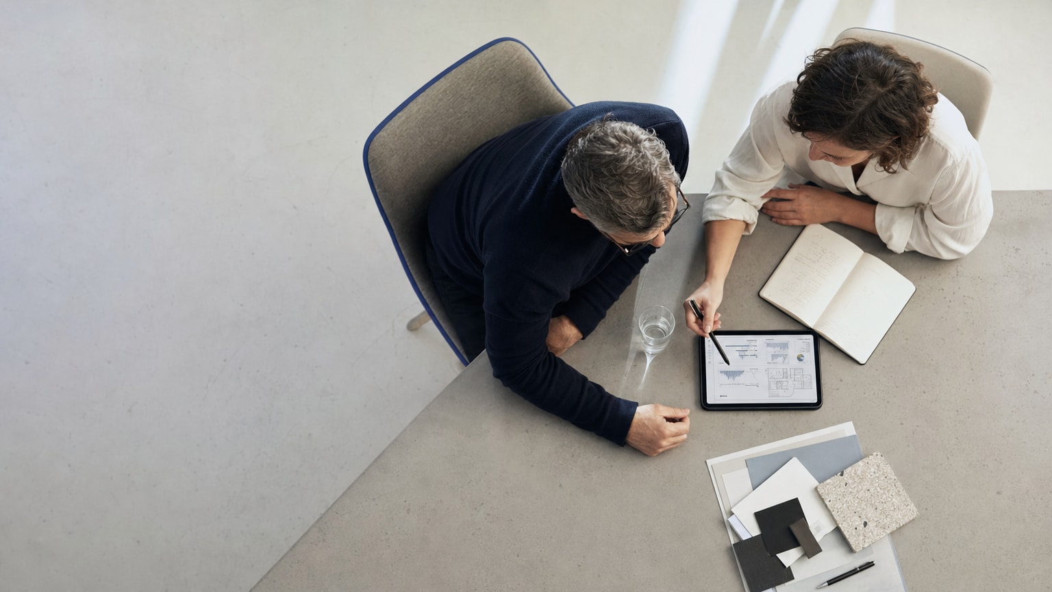 Zwei Personen, ein KMU-Geschäftsführer und ein Agentur-Berater, sitzen an einem modernen Besprechungstisch und blicken konstruktiv auf ein Tablet, auf dem Diagramme und Projektpläne zu sehen sind. Die Atmosphäre ist professionell und partnerschaftlich.