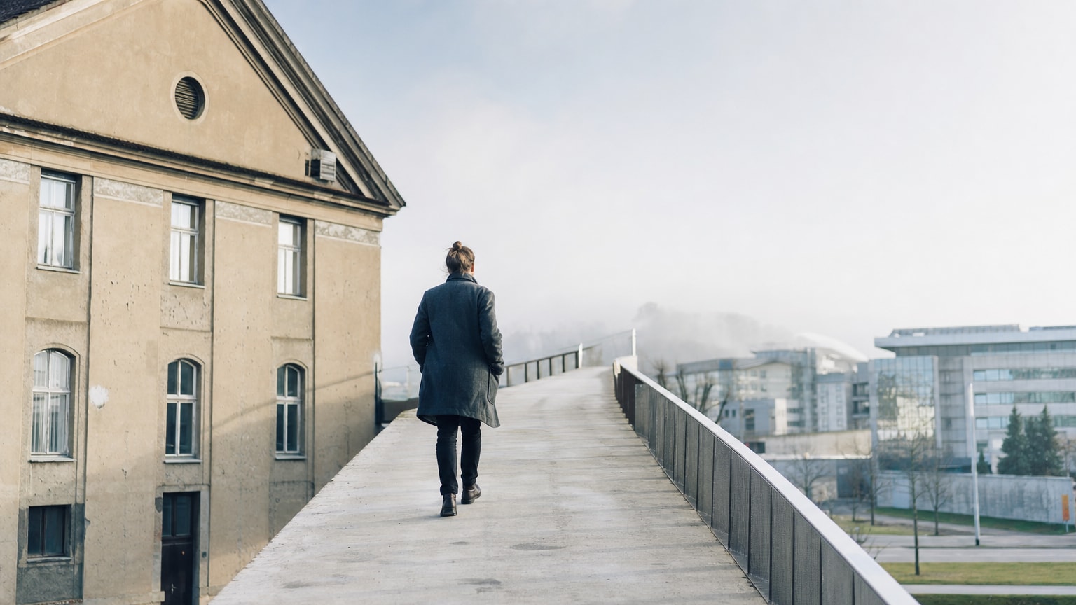 Abstraktes, helles Bild eines aufsteigenden Pfades oder einer Brücke, die von einem traditionellen Betriebsgebäude in eine lichtdurchflutete, moderne digitale Landschaft führt — symbolisch für den Weg vom Status quo in eine digitalisierte Zukunft.