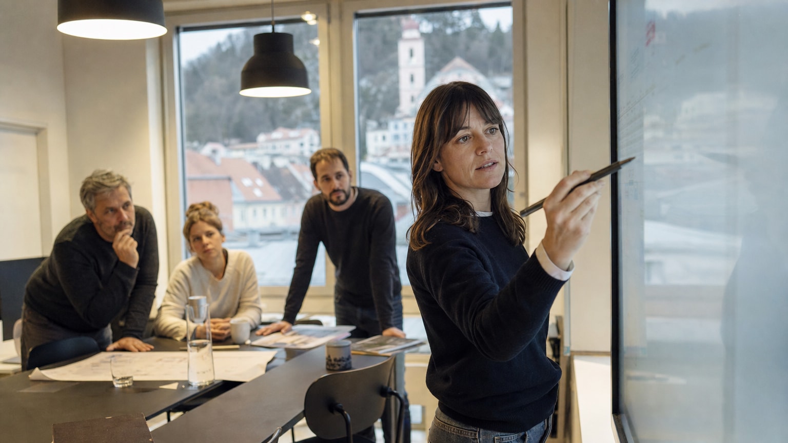 Ein kleines Team aus Agentur-Fachleuten und KMU-Inhabern arbeitet gemeinsam an einem digitalen Workflow auf einem großen Bildschirm in einer modernen, aber bodenständigen Büroumgebung – warme Lichtstimmung, österreichische Kleinstadt durch das Fenster sichtbar.