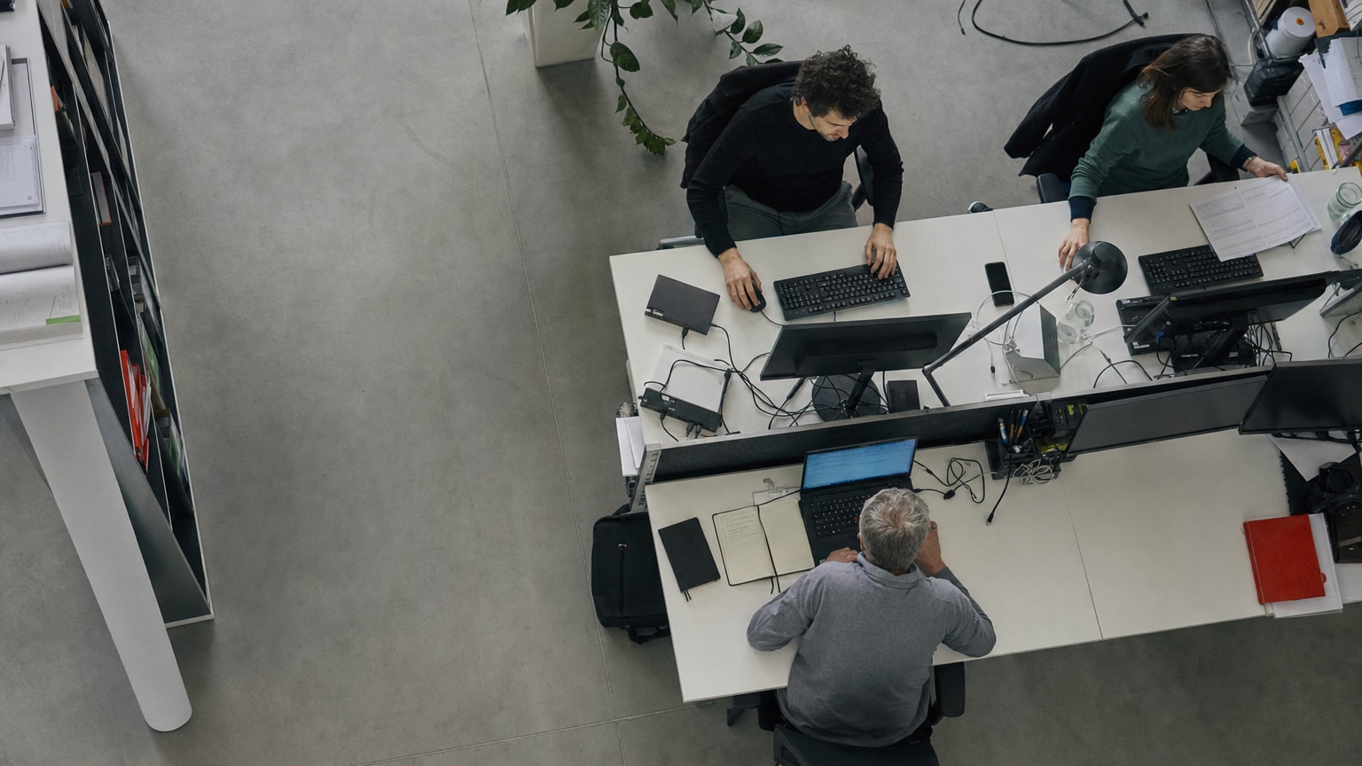 Stilisierte Darstellung eines mittelständischen Büros, in dem mehrere digitale Prozesse nahtlos ineinandergreifen – Zahnräder, Datenströme und ein Team, das konzentriert an Bildschirmen arbeitet, während im Hintergrund automatisierte Workflows visualisiert werden.