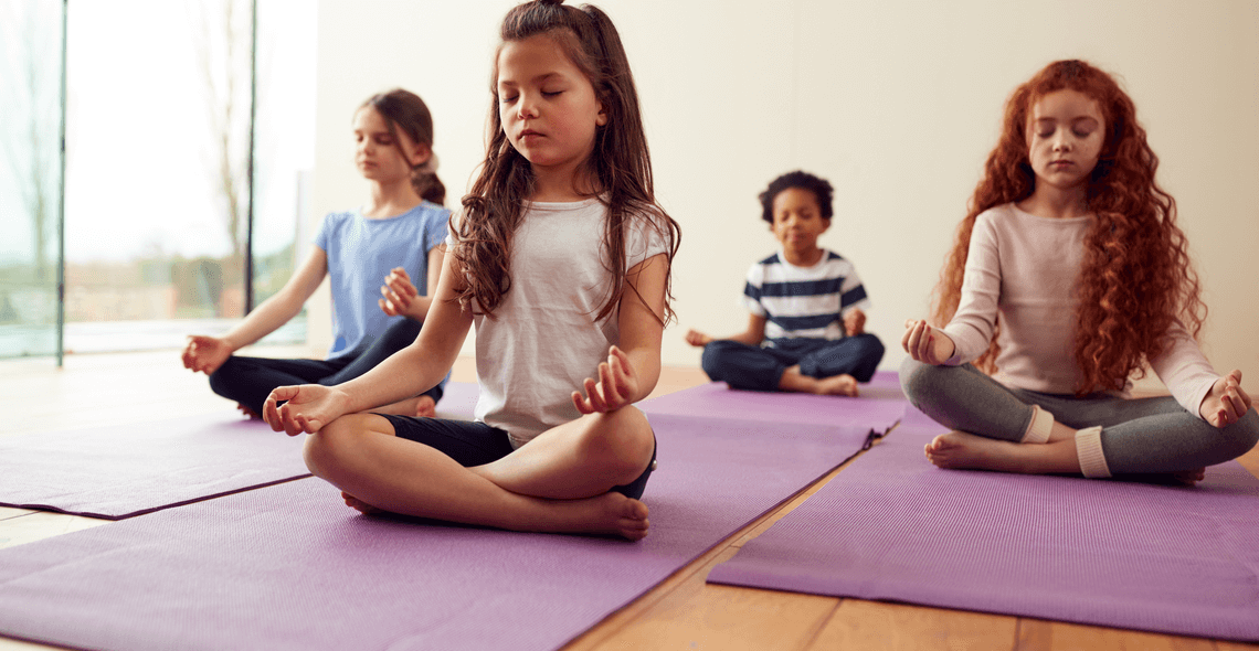 Children sitting cross-legged on purple yoga mats practising mindfulness meditation