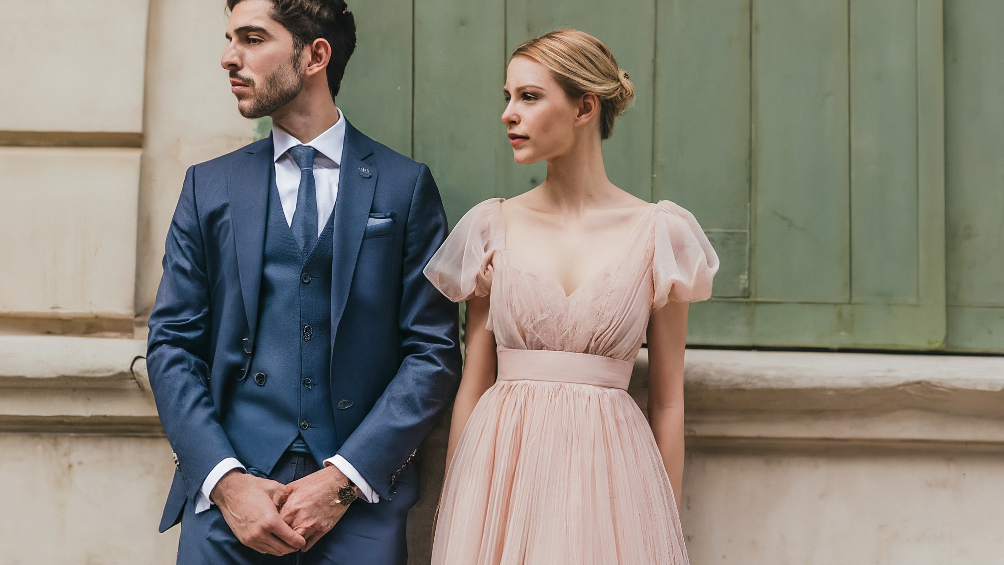 Due lama bianchi in stile cartoon, un maschio elegante con completo blu e una femmina elegante con vestito rosa, sorridono leggermente e guardano verso l'osservatore, sfondo sfocato con grafici verdi e rossi di criptovalute.