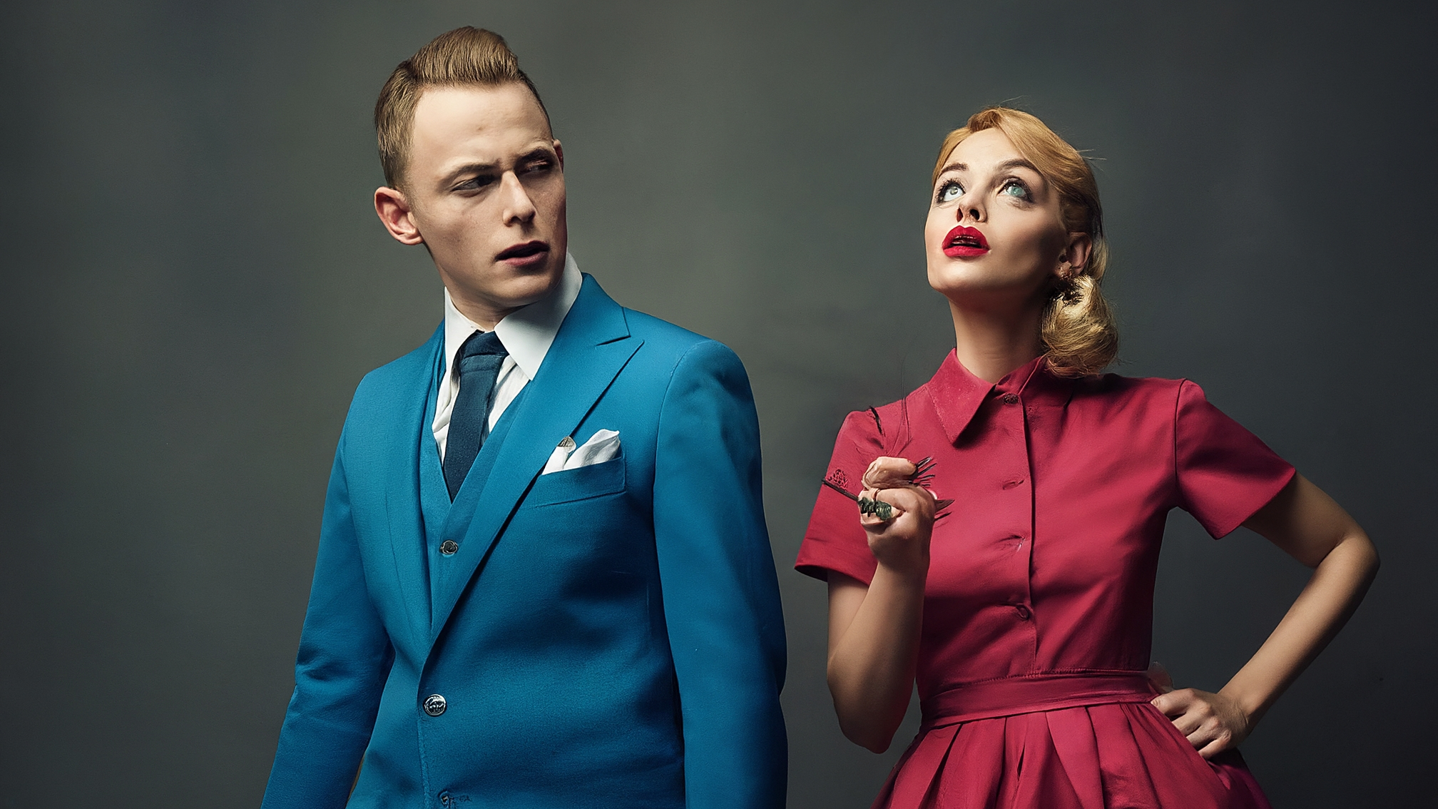 Due lama bianchi in stile cartoon con vestiti eleganti (uno maschio in completo blu, una femmina in vestito rosa), espressione seria ma incuriosita, uno guarda verso l'alto con un punto interrogativo stilizzato sopra, l'altra tiene in mano una lente d'ingrandimento. Nessun testo. Colori vivaci ma professionali, con un tocco dorato per richiamare