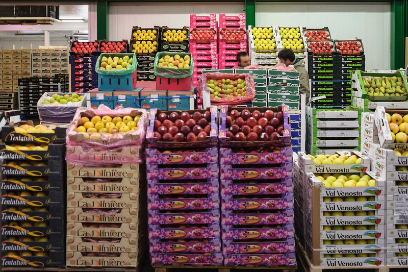 Stacked crates of apples and pears in branded cartons on a wholesaler's stall at the Rungis market, sorted by variety and size
