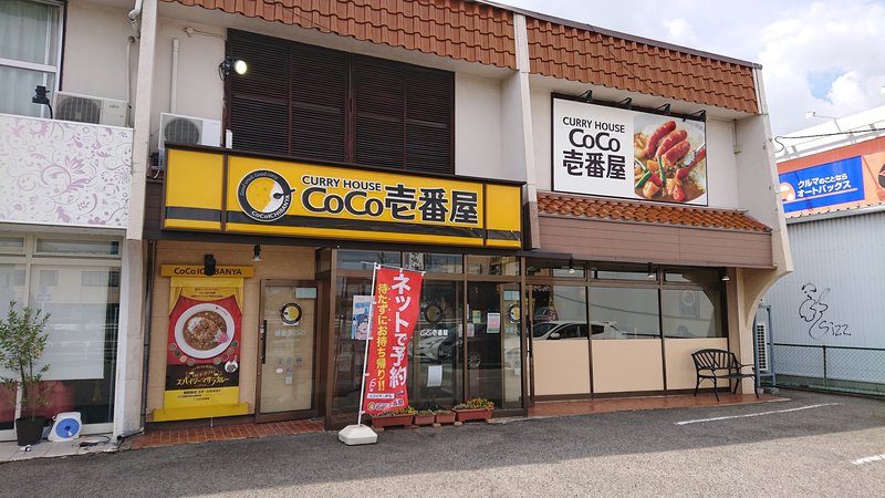 The yellow-signed storefront of a Curry House CoCo Ichibanya restaurant in Kasugai, Aichi prefecture, with a red takeaway-ordering banner by the entrance